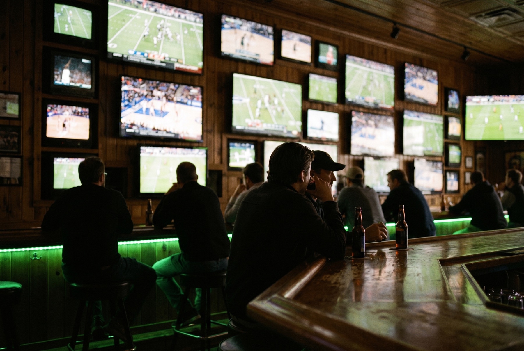 A wall of glowing screens shows every game over the green-lit bar rail